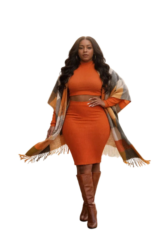 Woman in an orange outfit with a plaid shawl standing on a sidewalk.