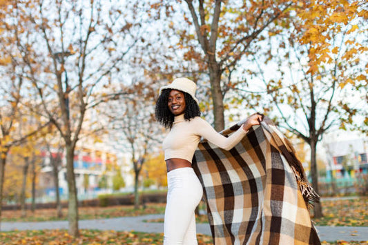 Woman with white two piece set, hat and plaid cardigan shows how to create a capsule wardrobe with versatile clothes that transition into fall and spring