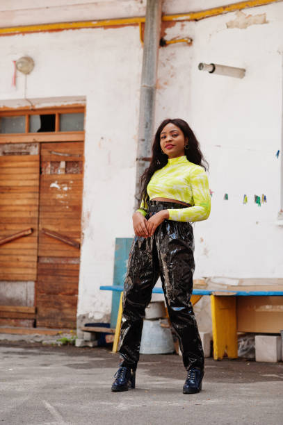 Black woman in bright yellow shirt and black leather pants with black booties fall and winter fashion