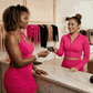 Two women in bright pink outfits interacting in a store setting.