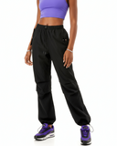 Person wearing a purple sports tank top black cargo parachute pants and black and purple air maxes on a white background