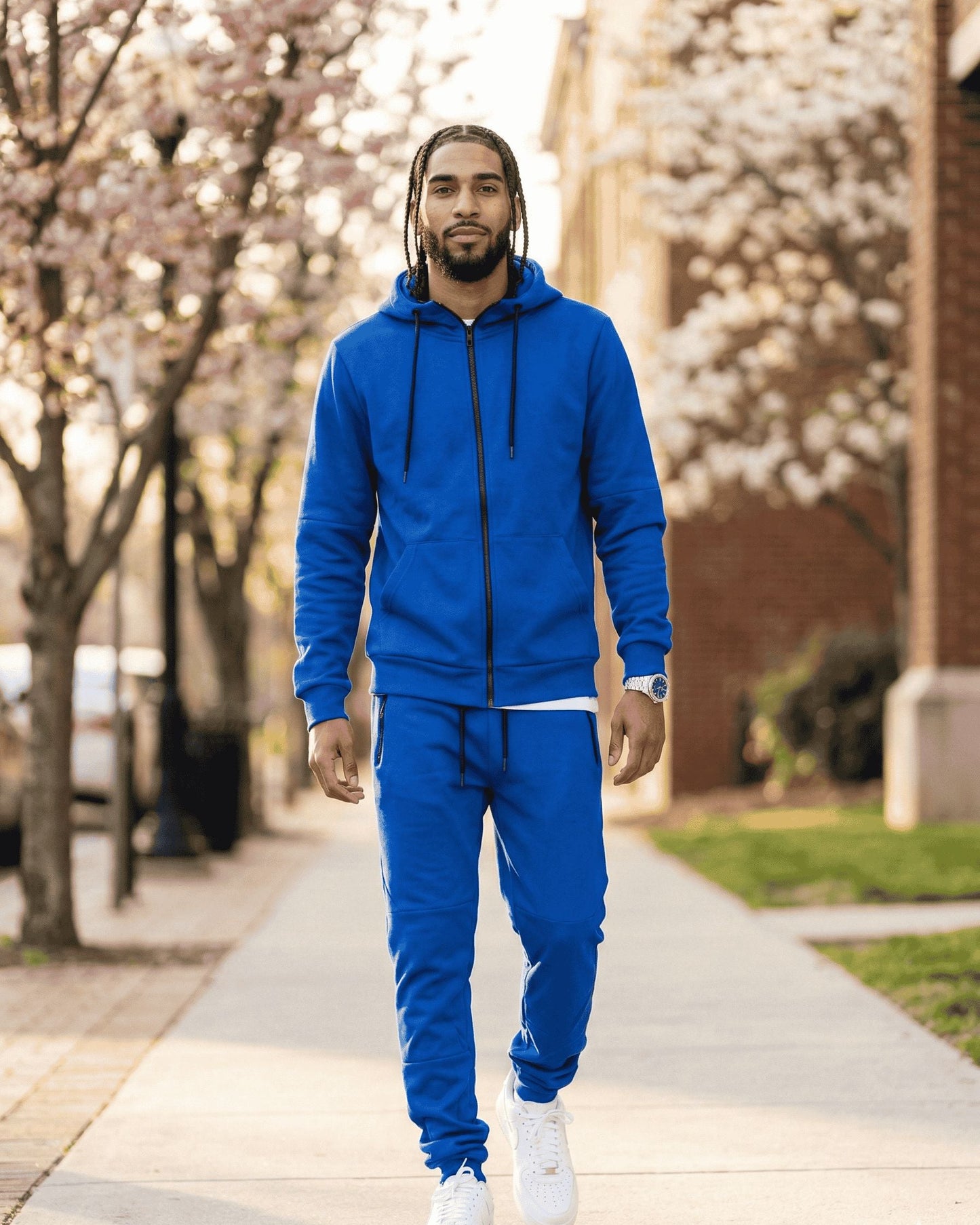 Man wearing a blue tracksuit walking on a sidewalk with cherry blossom trees in the background