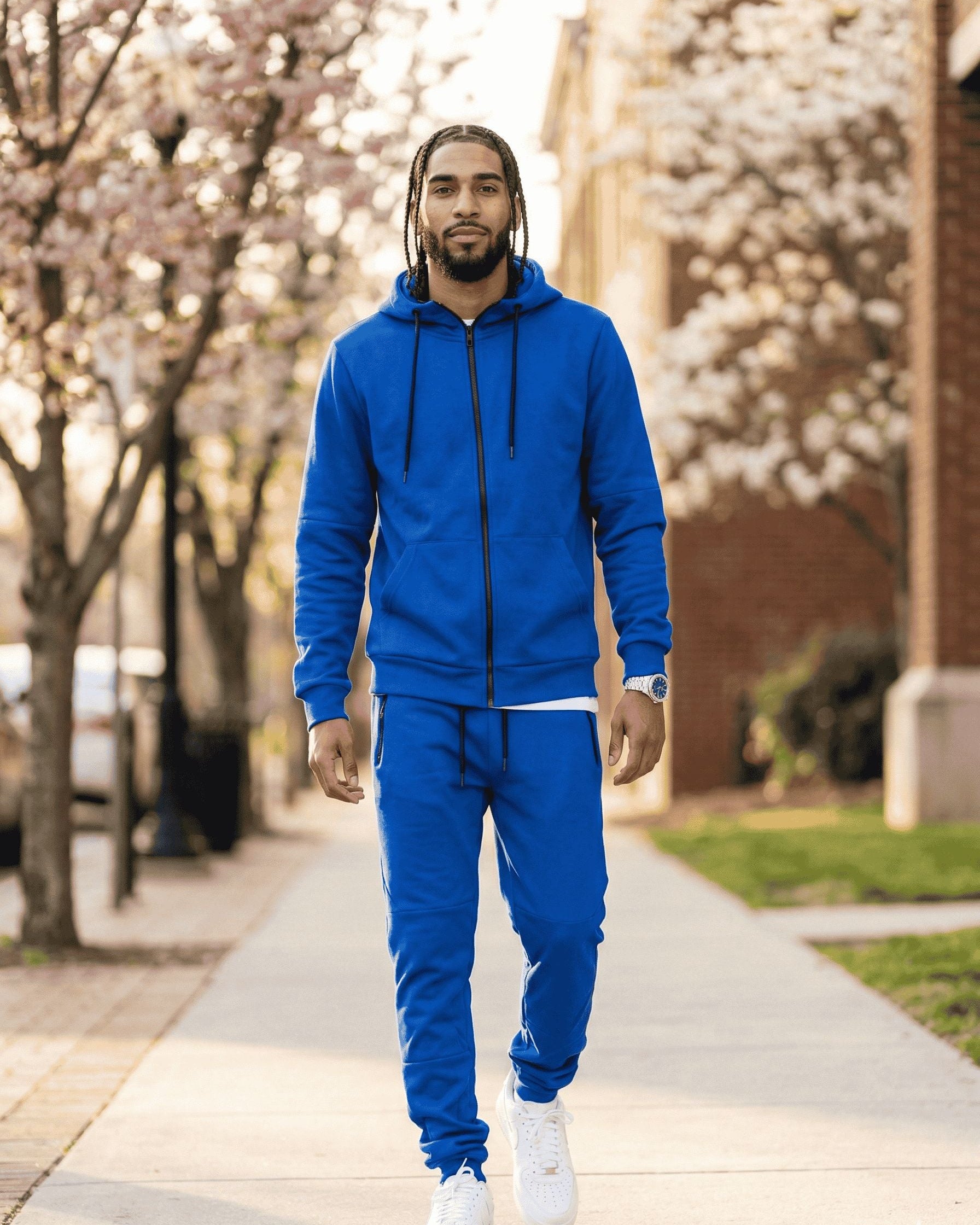 Man wearing a blue tracksuit walking on a sidewalk with cherry blossom trees in the background