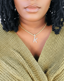 Person wearing a gold necklace with a 'K' pendant, wearing a green sweater.