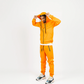 Orange men’s tech fleece matching set worn post-workout at gym, Yeezy Wave Runners visible, relaxed confident look.