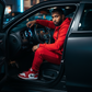 Red men’s tech fleece tracksuit styled with Jordan 1s, night lifestyle photo of black man sitting inside matte black Dodge Charger SRT.