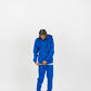 Side-angle view of royal blue men’s matching sweatsuit with hands in pockets, white background.