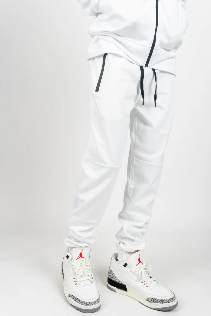 White men’s tech fleece tracksuit with black zipper details, styled with white and red Jordans on white studio background.
