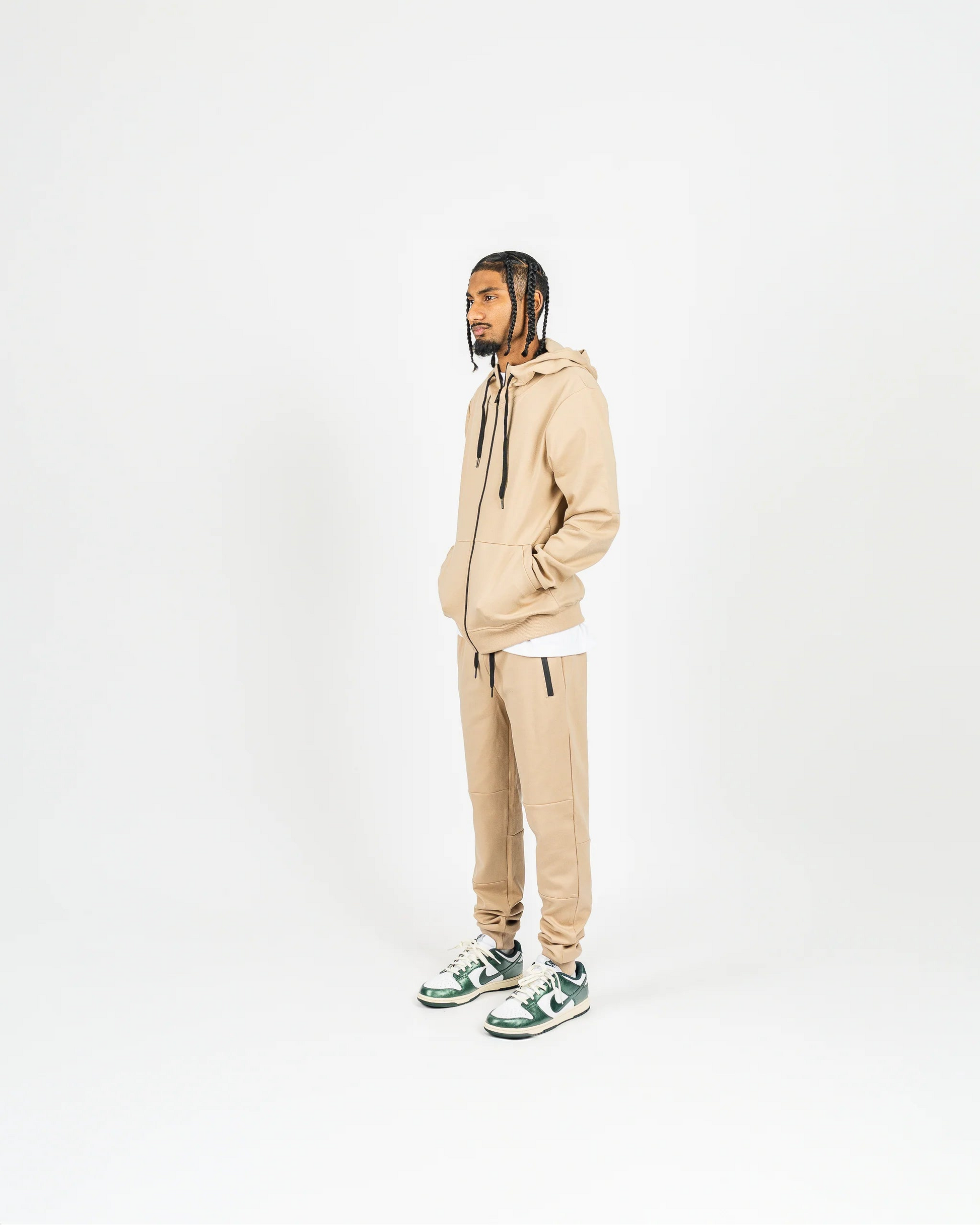Side-angle studio shot of nude men’s matching sweatsuit with hood up and minimal background, relaxed streetwear vibe.