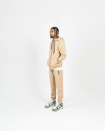 Side-angle studio shot of nude men’s matching sweatsuit with hood up and minimal background, relaxed streetwear vibe.