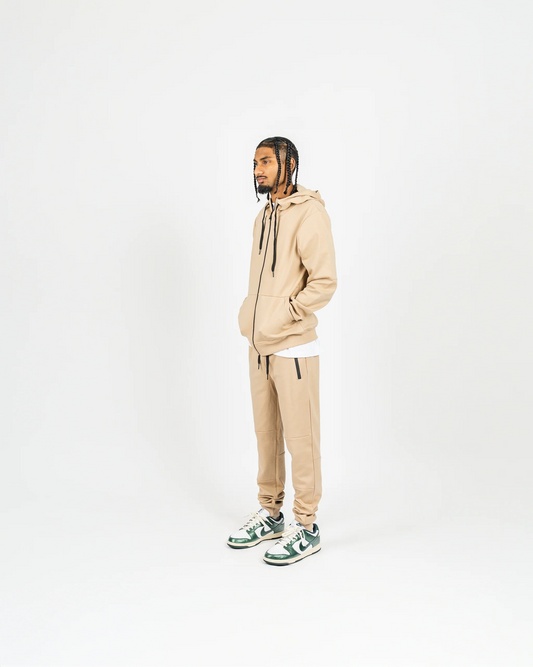 Side-angle studio shot of nude men’s matching sweatsuit with hood up and minimal background, relaxed streetwear vibe.