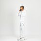 White men’s tech fleece tracksuit with black zipper details, styled with white and red Jordans on white studio background.