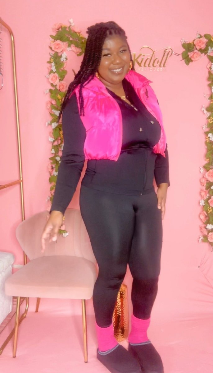Plus-size woman wearing black matching set with pink puffer vest, pink slouch socks, and black UGG slides for cozy fall and winter outfit