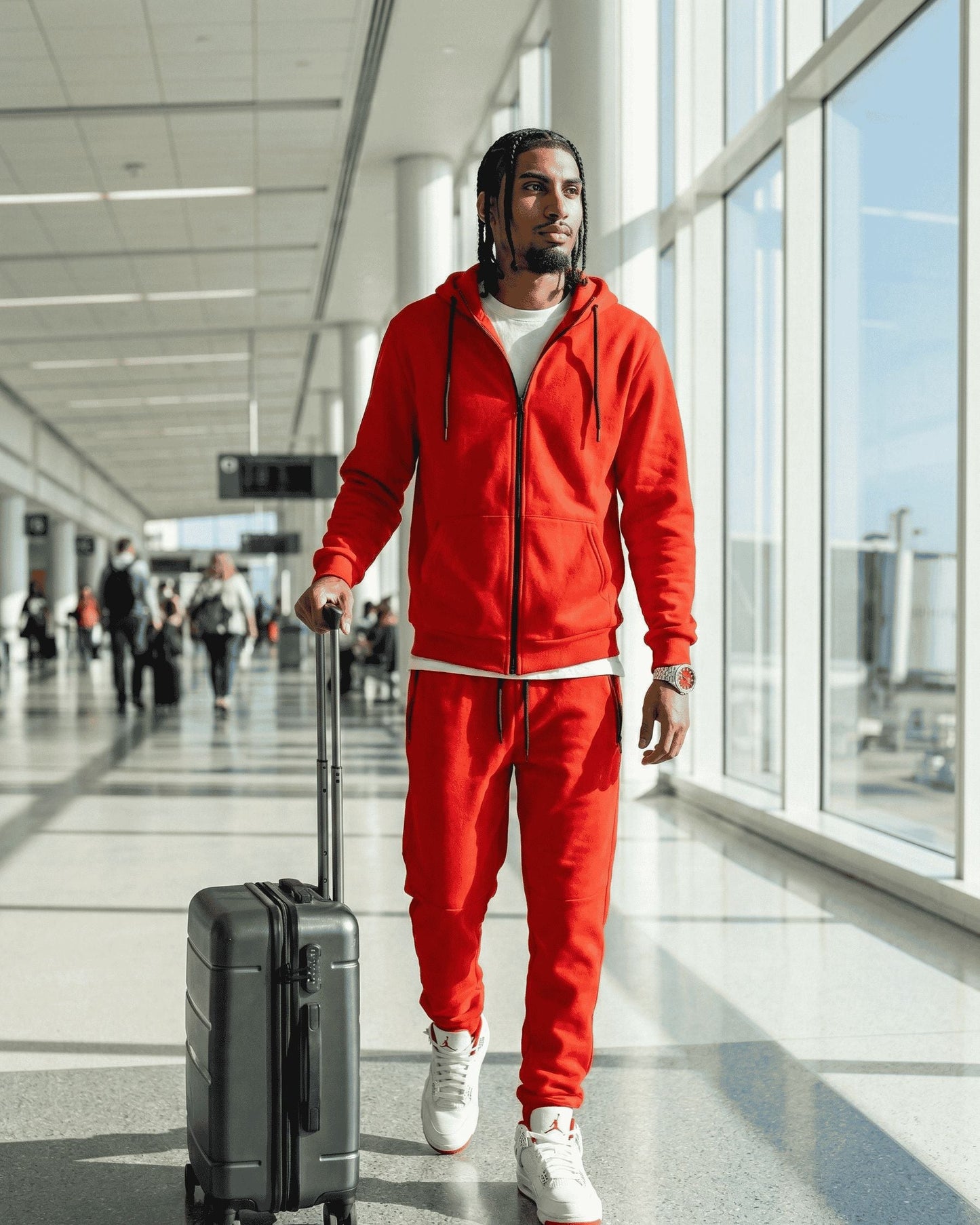 Man in red tracksuit pulling a suitcase in an airport terminal