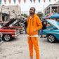 Person in orange tracksuit standing in front of classic cars at a car show.