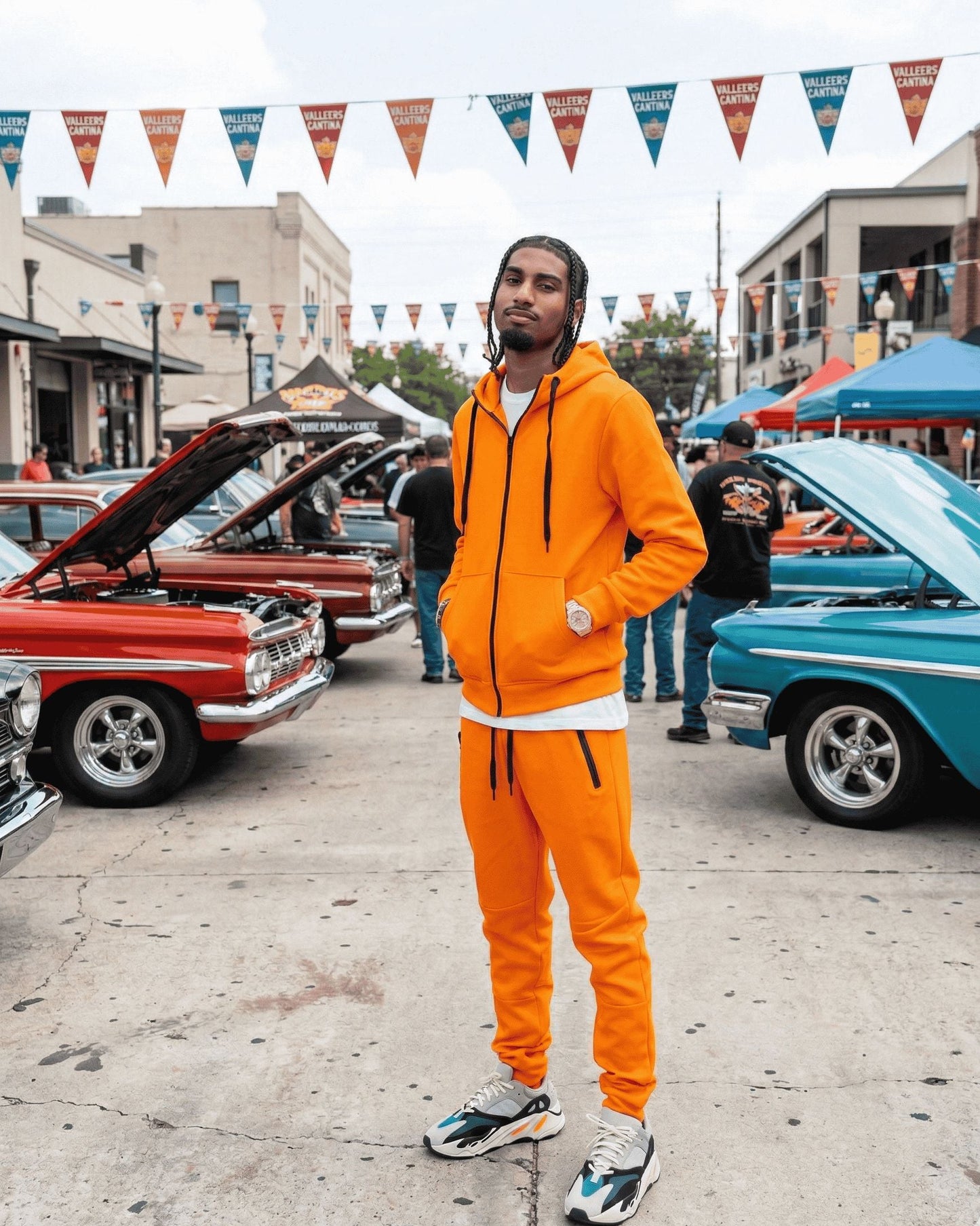 Person in orange tracksuit standing in front of classic cars at a car show.