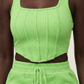 Person wearing a bright green ribbed tank top and skirt set against a neutral background