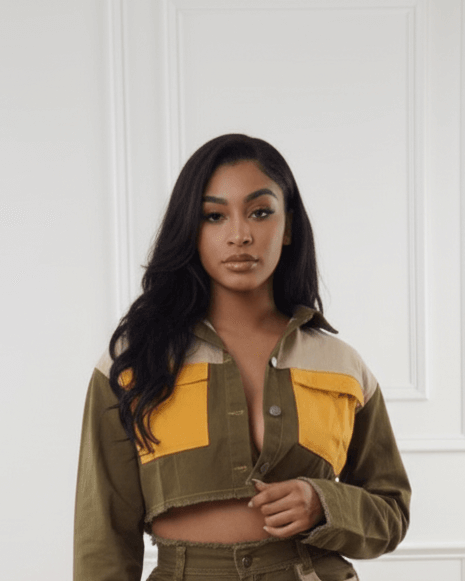 Woman wearing a patchwork jacket and shorts with a white wall background