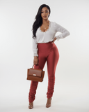 Woman wearing a white top and orange rust pants holding a brown handbag on a white background