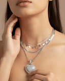 Woman wearing a silver necklace with a heart-shaped pendant against a neutral background