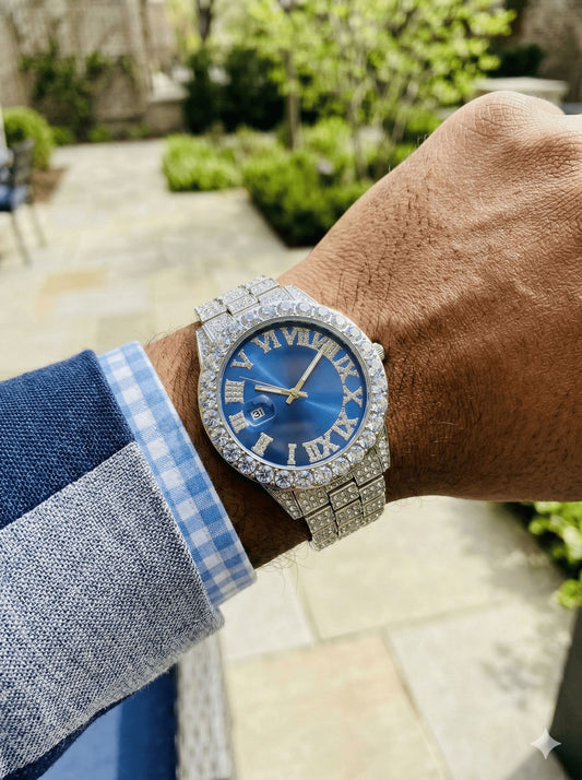Luxury watch with blue face and diamond accents on a wrist, outdoor background