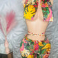 Colorful tropical print romper outfit on a mannequin against a textured white wall.